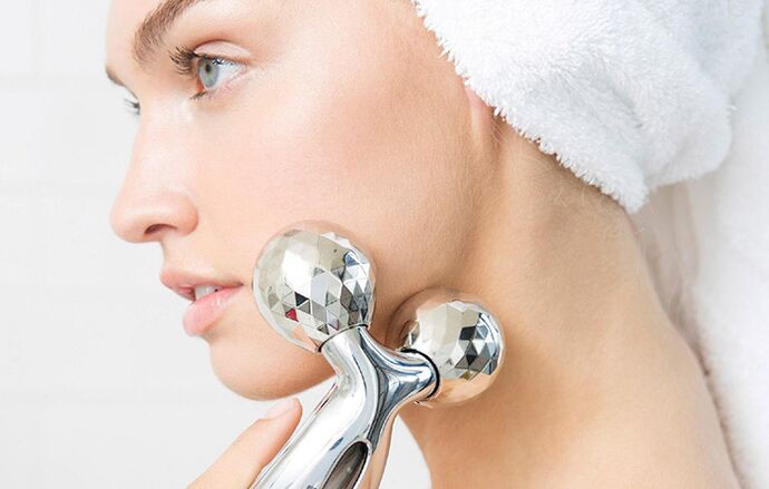 A girl rejuvenates her face with a mechanical roller massager. 